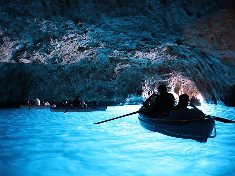 A rowboat carrying four passengers across the lit water inside the Blue Grotto