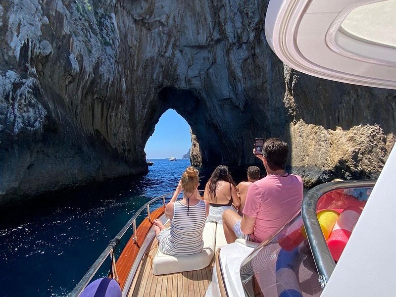 A boat nosing through a low rock arch, passengers looking up at the roof