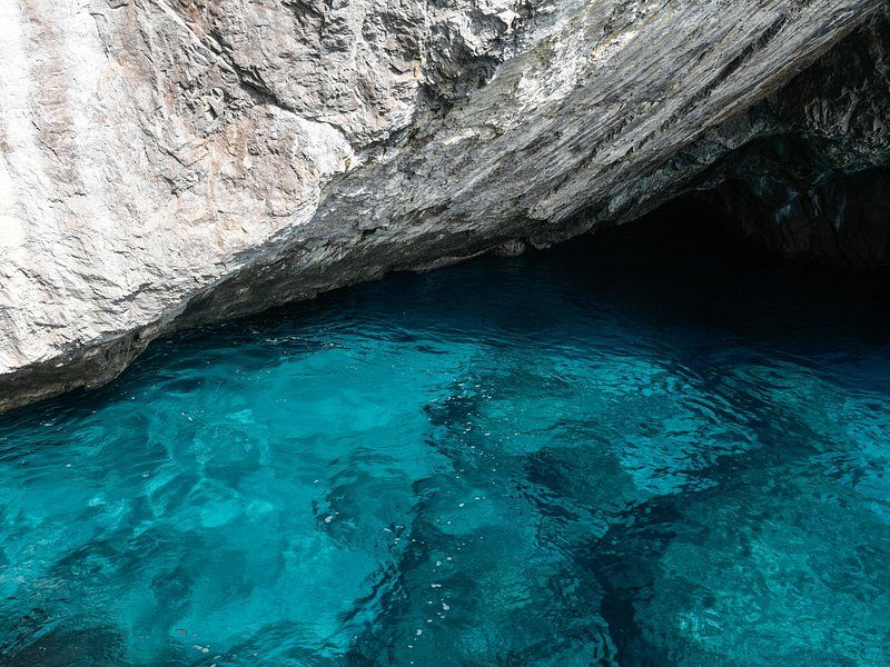 Clear turquoise water over pale rock at the foot of a limestone cliff