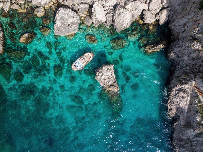 A small boat inside a turquoise cove ringed by limestone cliffs, seen from above