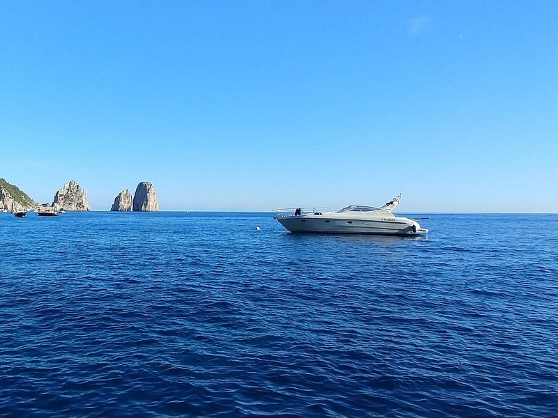 The Faraglioni seen from open water, with a motor yacht at anchor